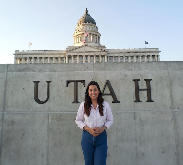 Capitol building with Utah sign and a woman smiling in front, symbolizing government transparency and policy engagement.