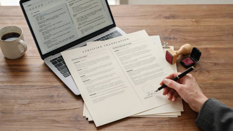Certified translation document signed by a human translator beside AI translation software on a laptop